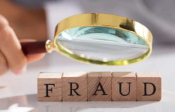 Investigator looking through a magnifying glass at wooden blocks with letters that read FRAUD