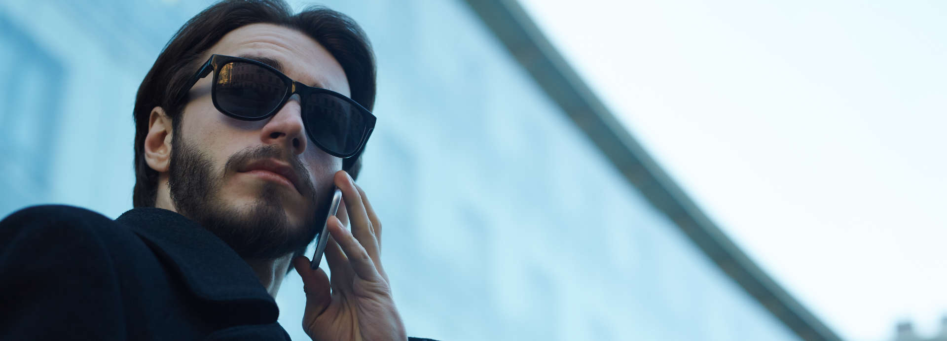 Beverly Hills private investigator in front of a building using a phone while observing the area through dark sunglasses