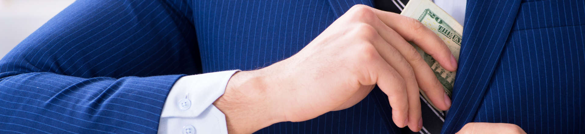 White-collar employee putting a pile of stolen banknotes into the inner pocket of his jacket