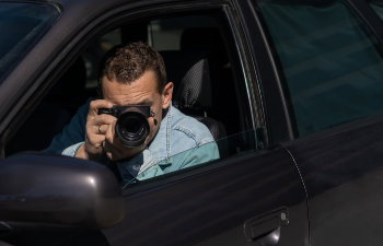 A person sitting inside a car points a camera out the window, focusing on something outside.