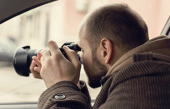 private detective sitting in car and taking photo with professional camera